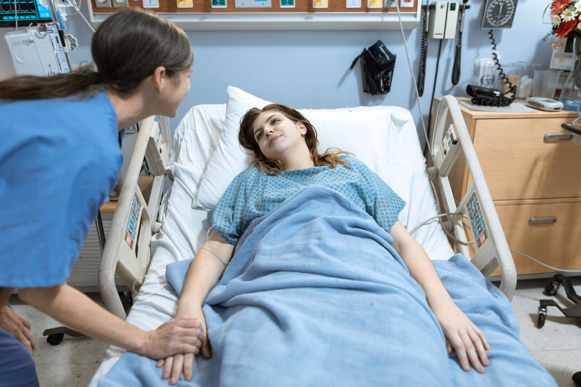Person in hospital bed being assisted by nurse