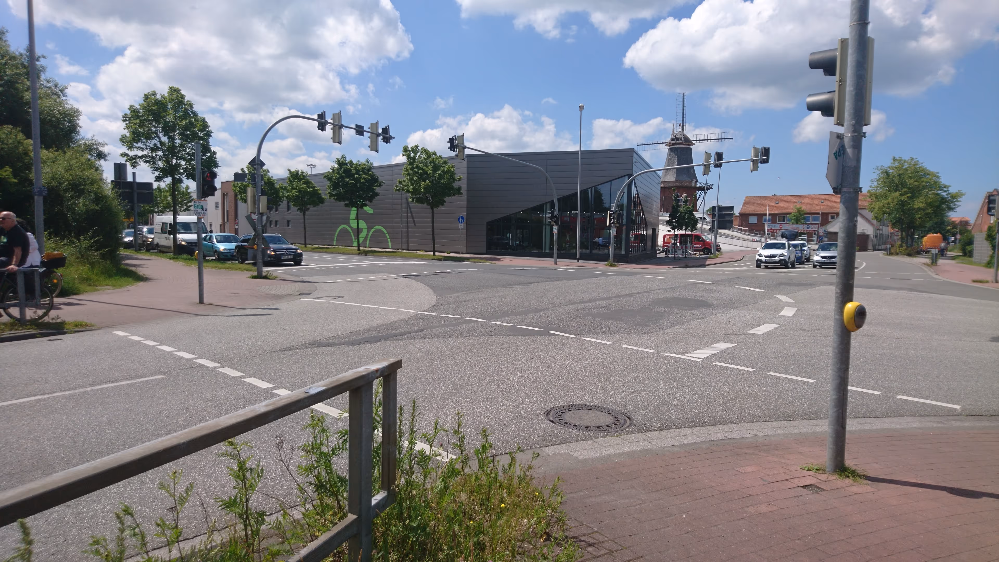 Kreuzung vor modernem Gebäude mit Windmühle im Hintergrund bei sonnigem Himmel.