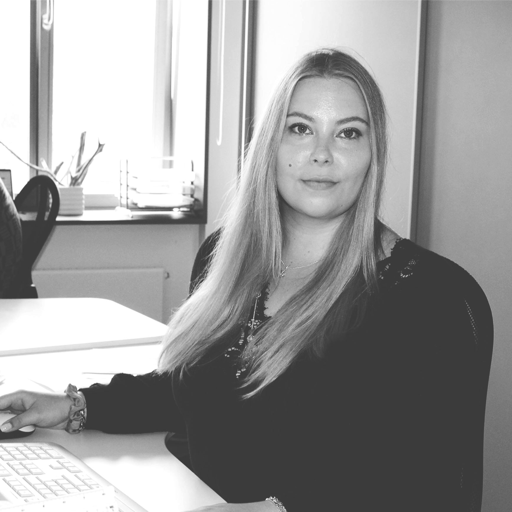 Frau mit langen Haaren am Schreibtisch im Büro, schwarz-weiß Bild.