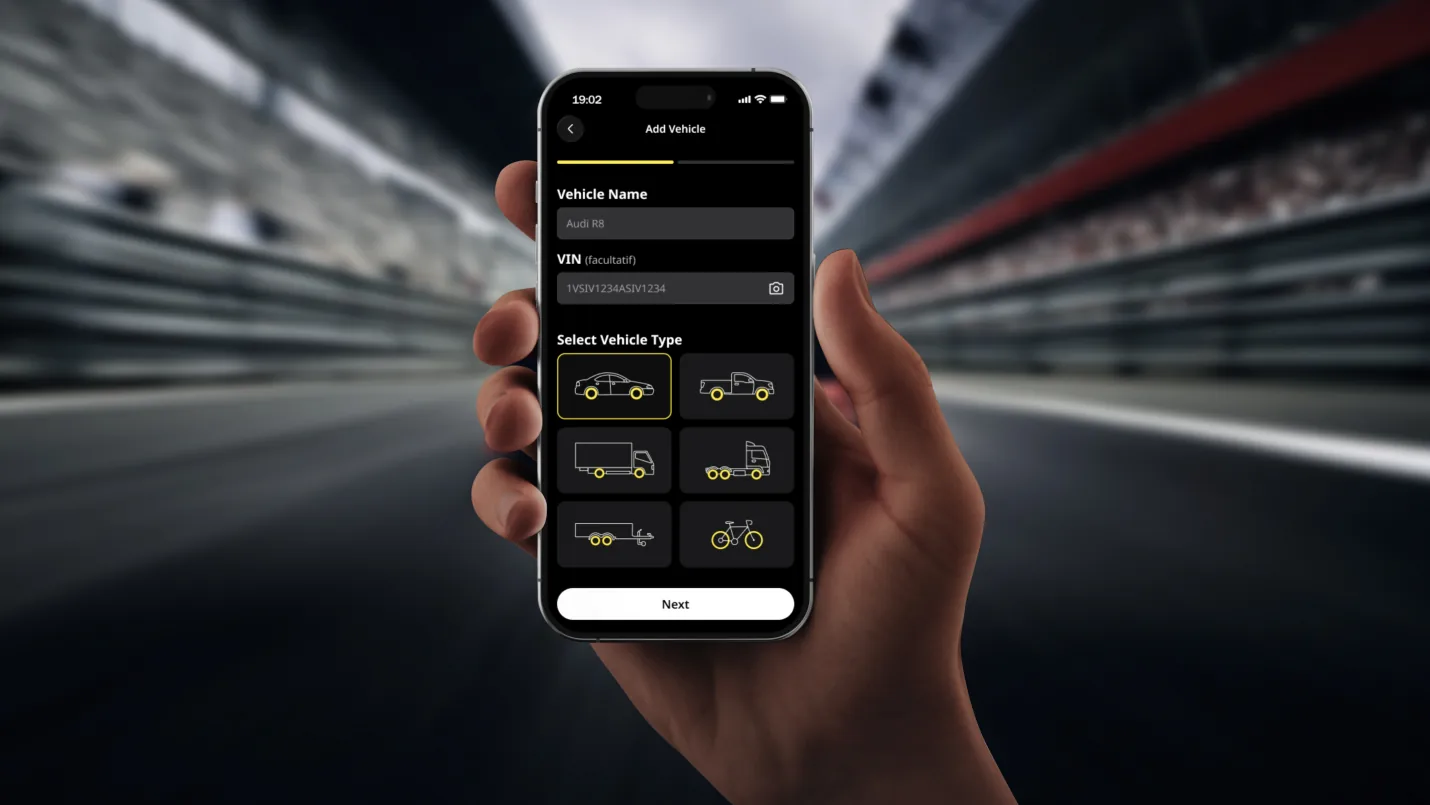 Main tenant un téléphone ouvert sur l'application MultiSync devant un circuit de course.