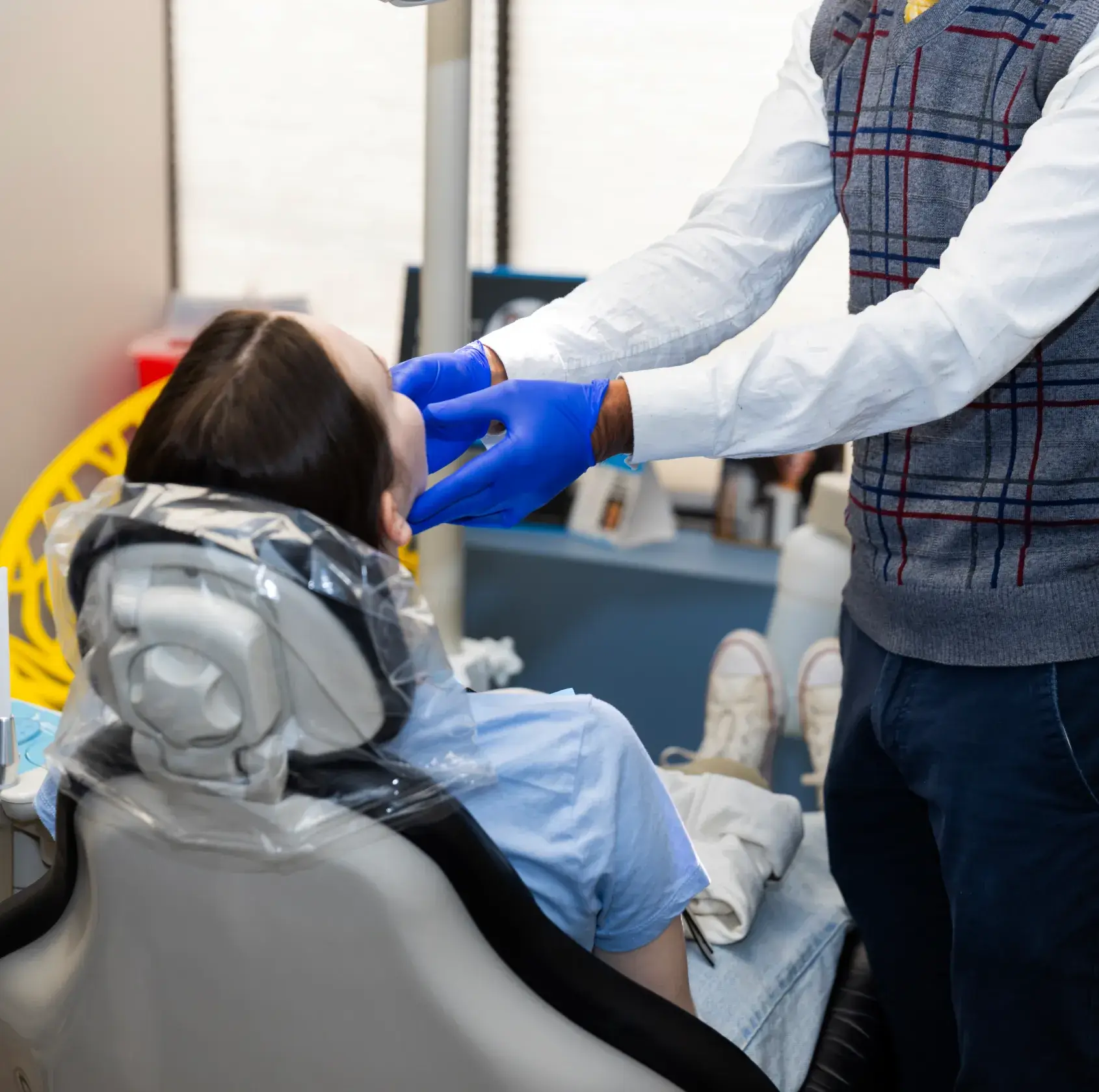 A dentist examines a patient's mouth while she sits in the dental chair.
