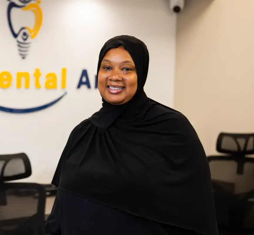 A woman in a black hijab smiles in an office setting with chairs in the background.
