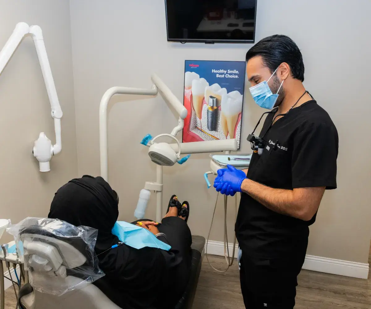 Dentist in protective gear discusses dental procedure with a patient in a dental clinic.