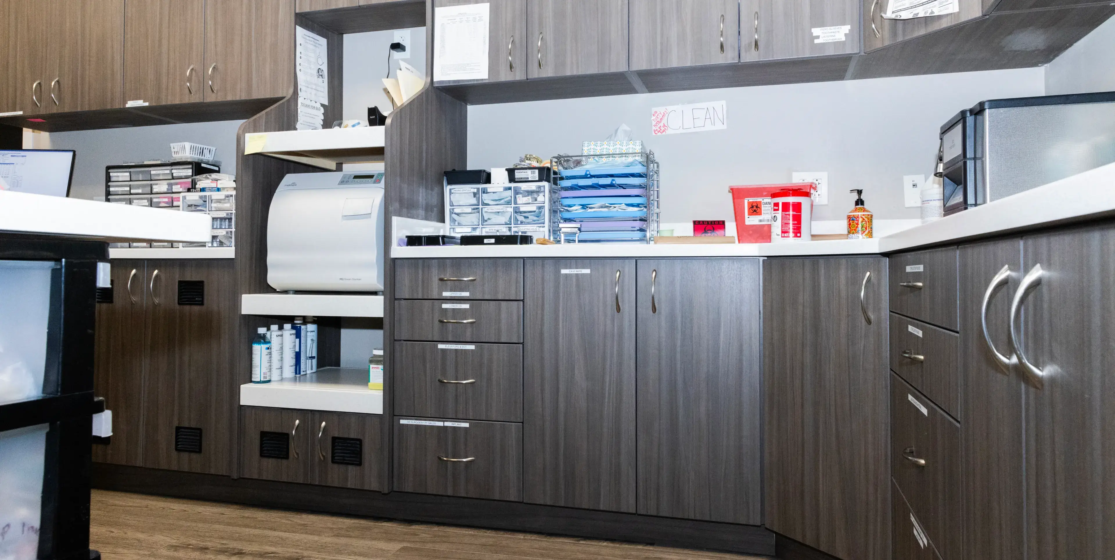 A clean, organized dental office lab with cabinets, a sterilization machine, and medical supplies on counters.