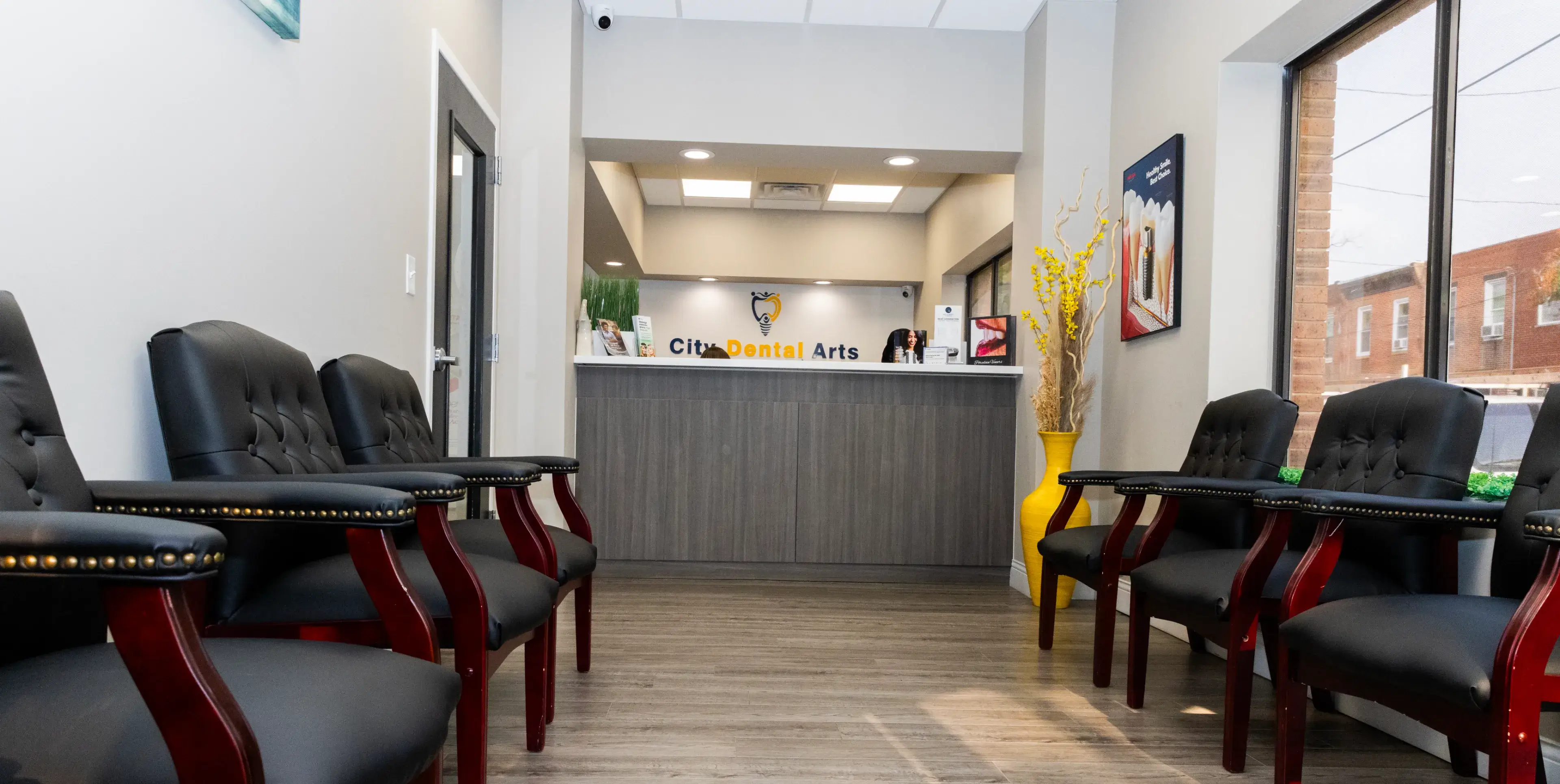 A dental office lobby with rows of black chairs and a front desk in the background.