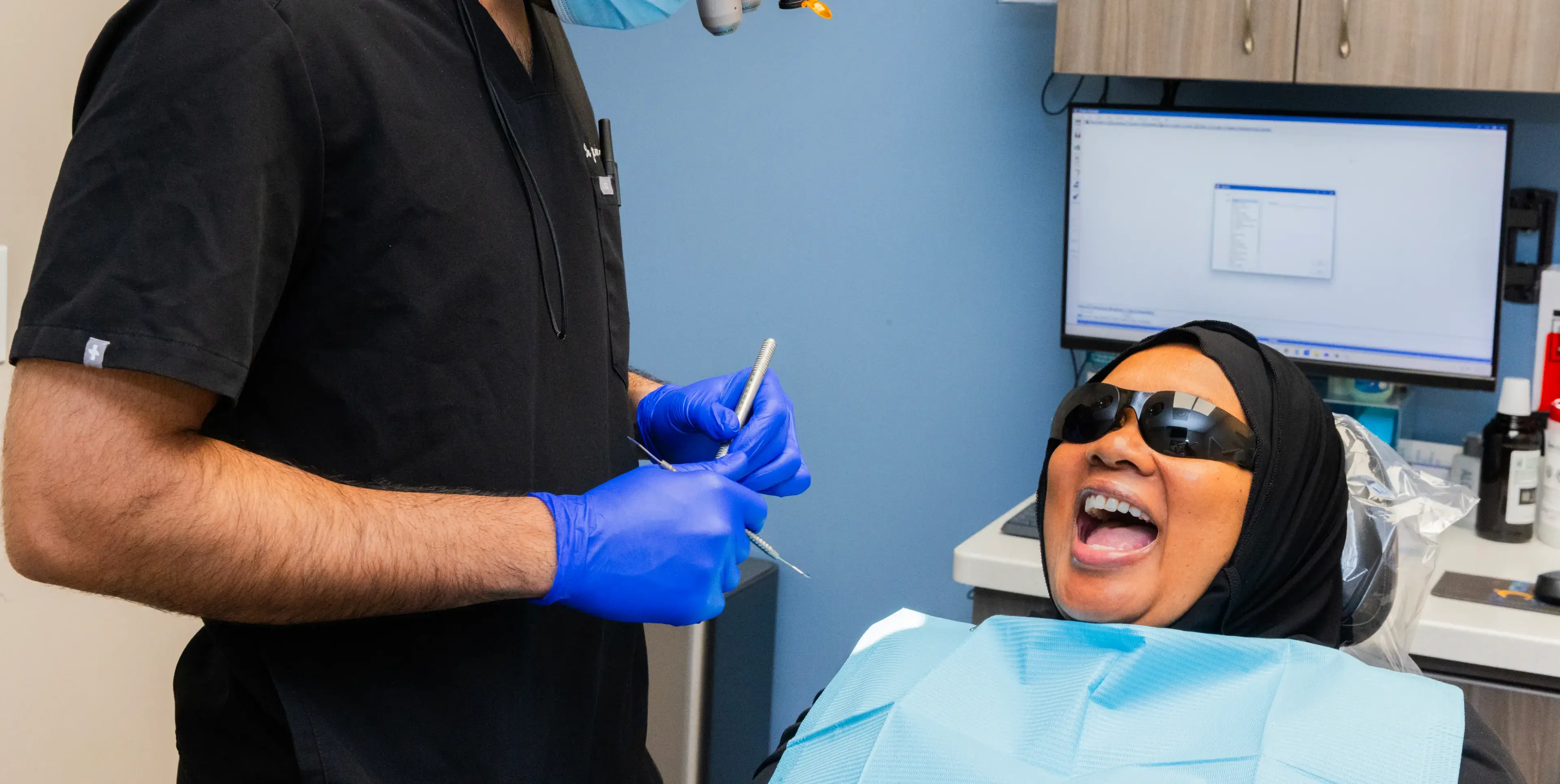 Dentist wearing gloves talks to a patient smiling in a dental chair.