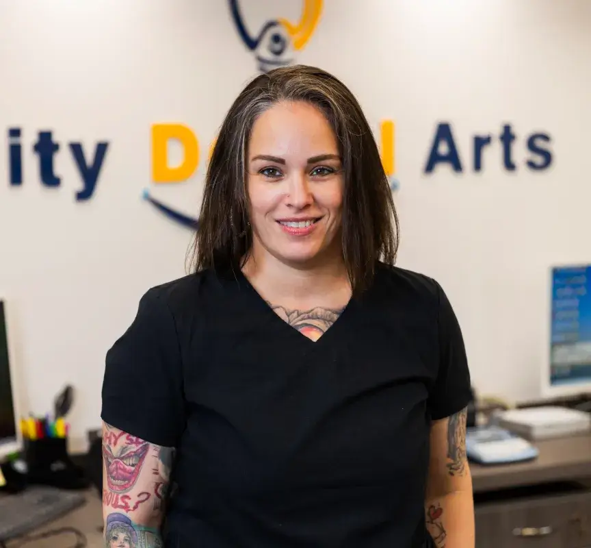A person in a black outfit stands smiling in a dental office.