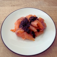 Sliced Salmon with Umami Everything On a white plate on a wood table.