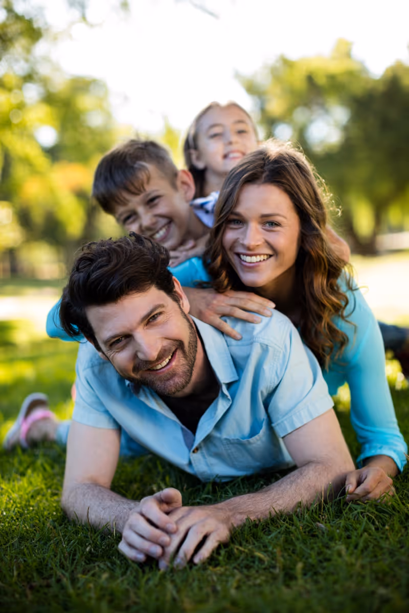 Happy family of four lying together on grass, smiling and embracing