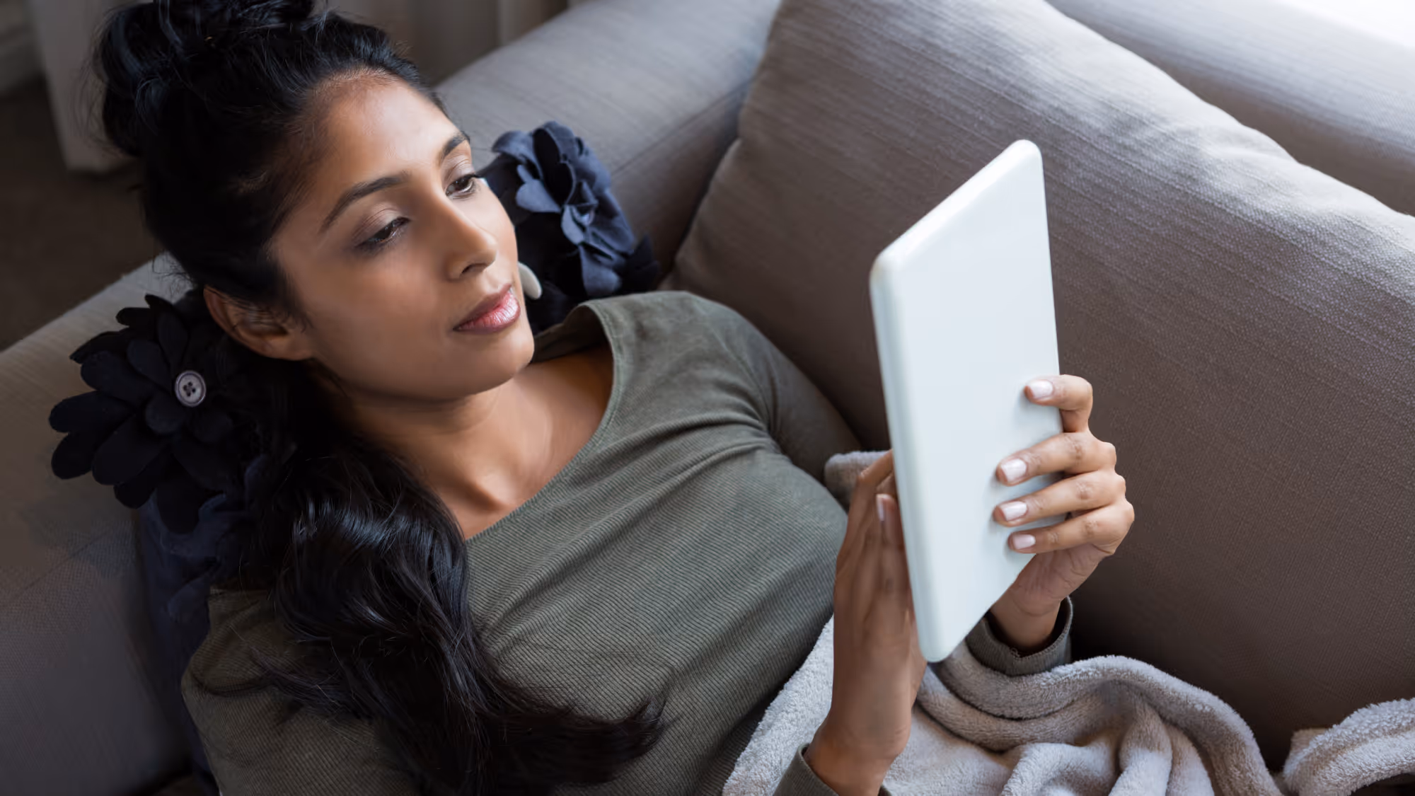 Woman relaxing on couch, using tablet with soft blanket nearby