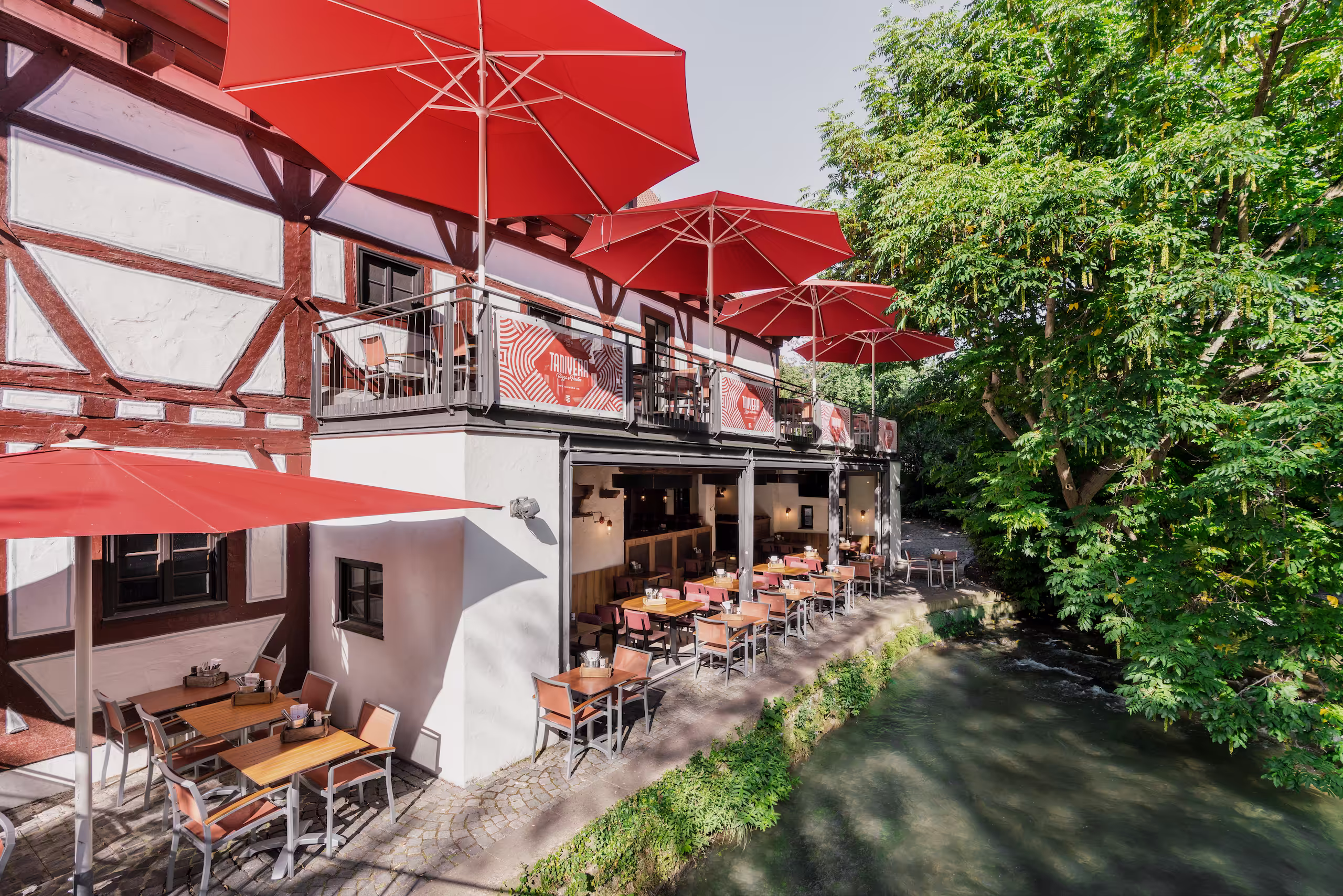 Terrasse mit roten Sonnenschirmen an der Blau neben einem Fachwerkhaus.