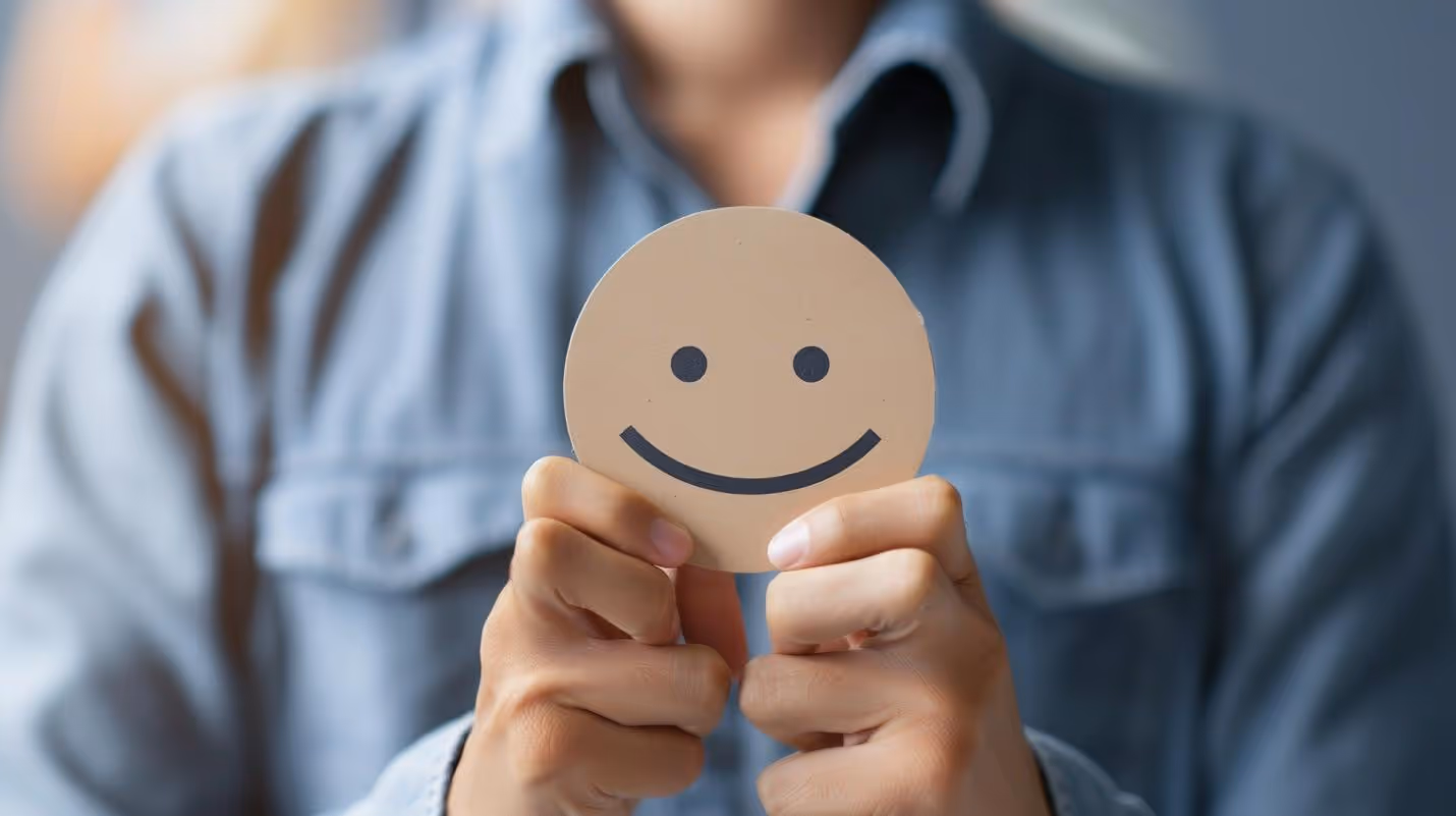 A person holding a paper with a smiley faceDescription automatically generated