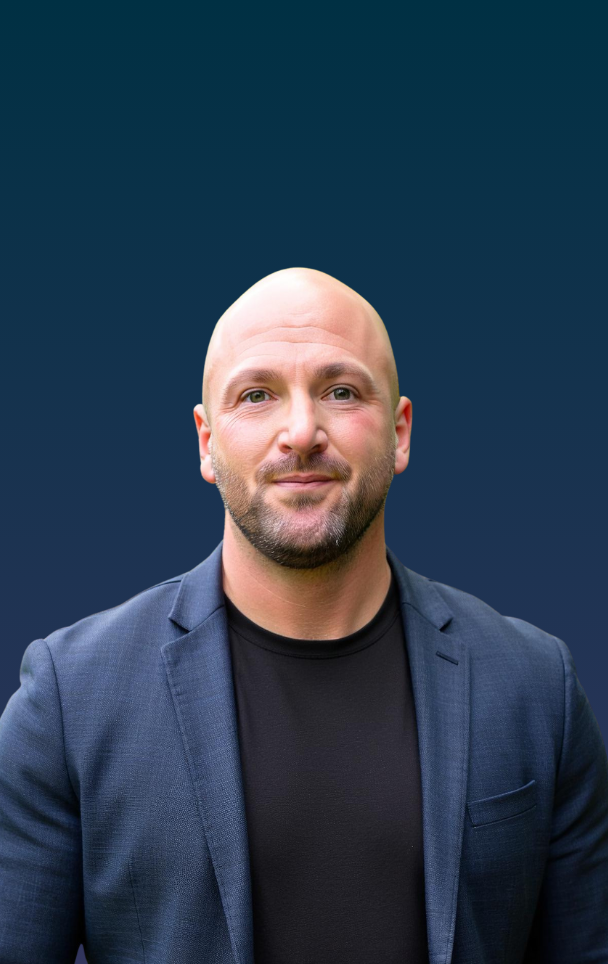 Portrait of a bald man wearing a navy blazer and black shirt against a dark blue background.