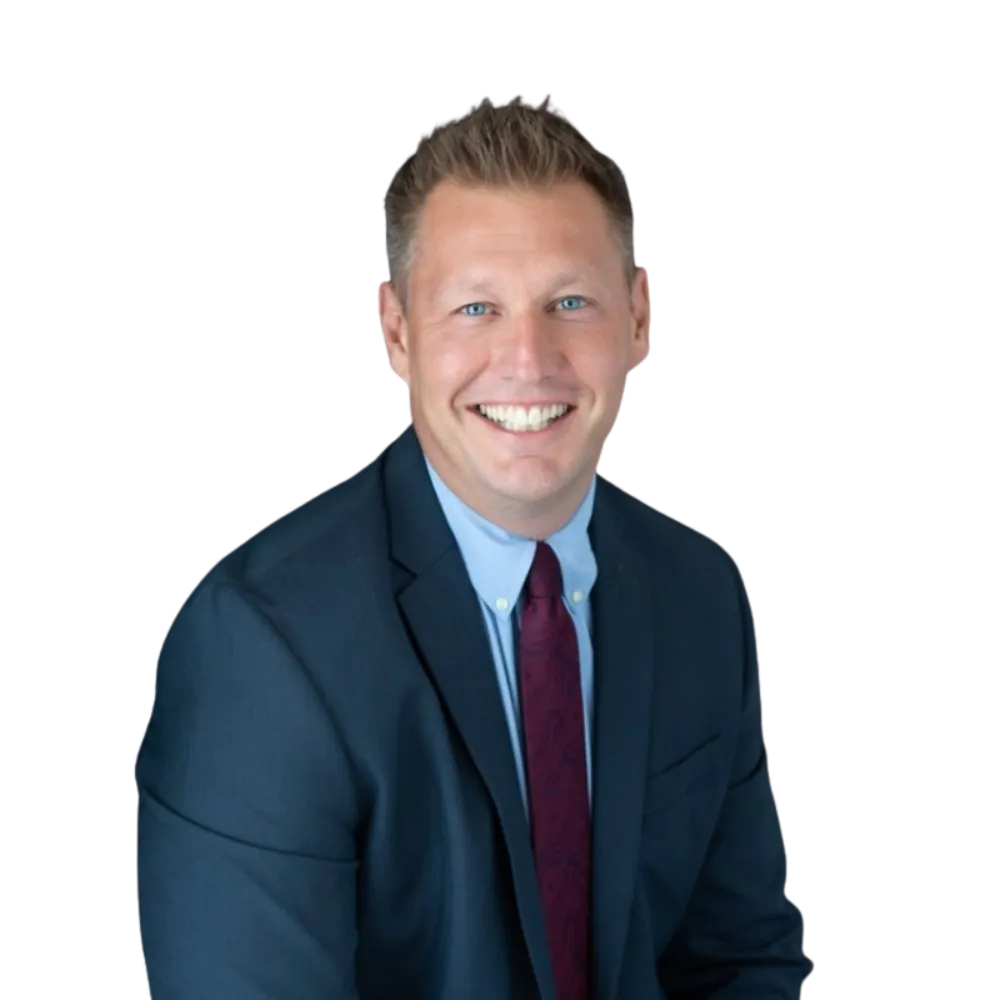 Head shot of a male smiling at the camera turned sideways in a dark suite with light blue dress shirt and deep read tie. 