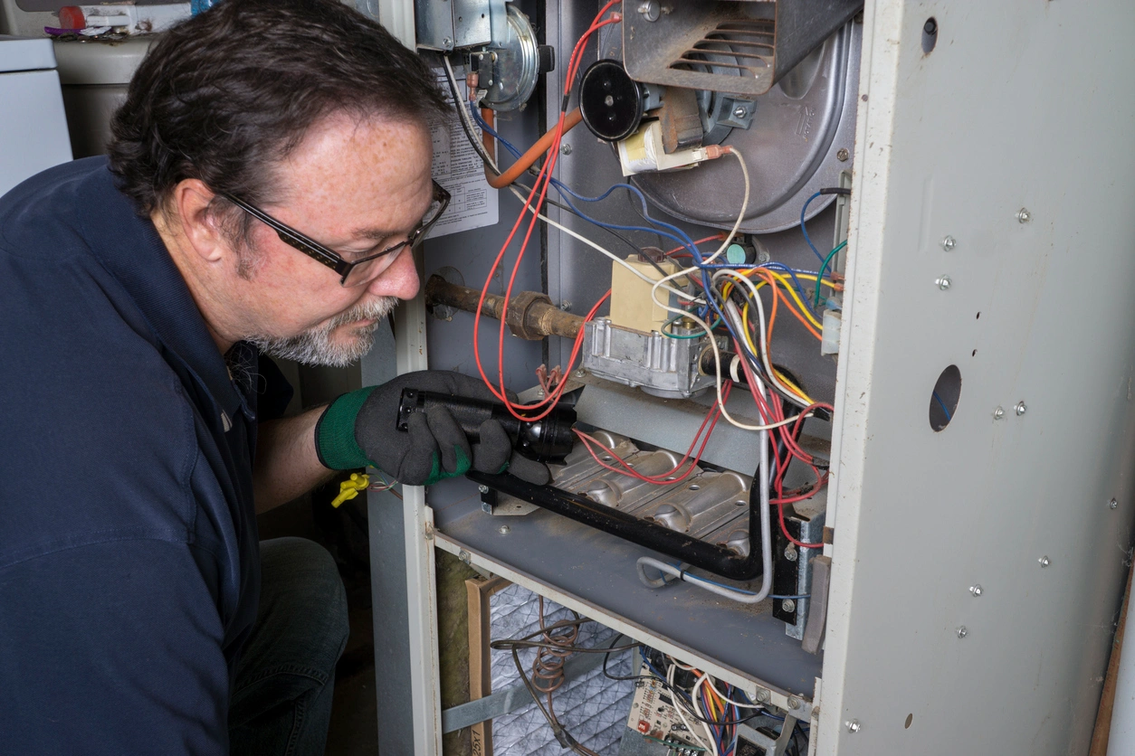 A man repairs a furnace in a home, focused on his work with tools nearby.