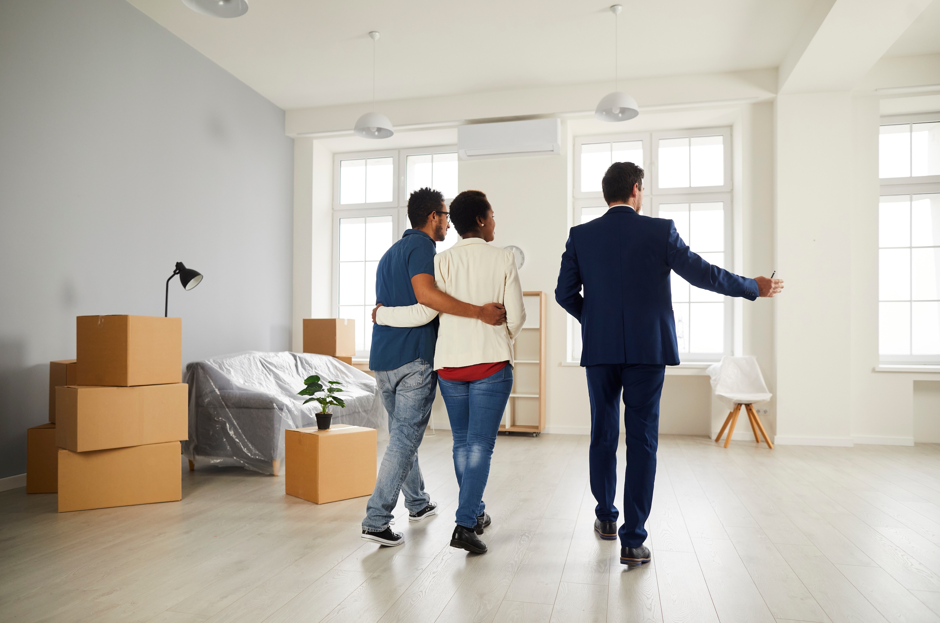 A leasing agent giving a tour of a spacious, unfurnished apartment with large windows and moving boxes, to a prospective couple at The Eleanor Daytona Beach in Daytona Beach, FL.
