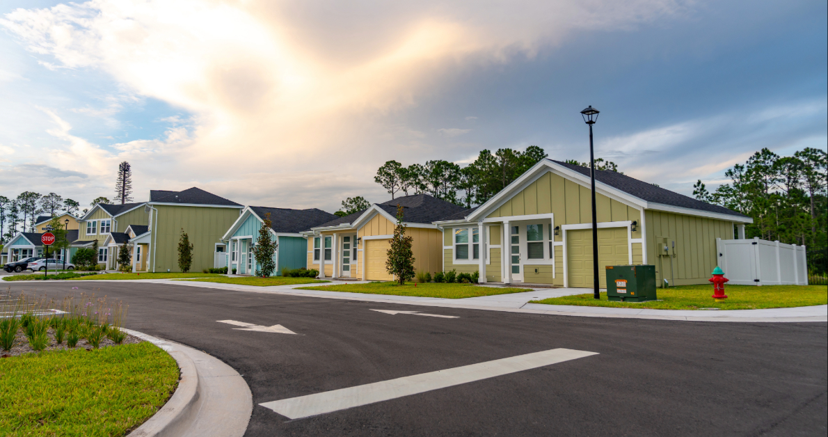 Exterior rendering of the modern clubhouse and apartment buildings with a curved driveway and palm trees at The Eleanor Daytona Beach in Daytona Beach, Florida.