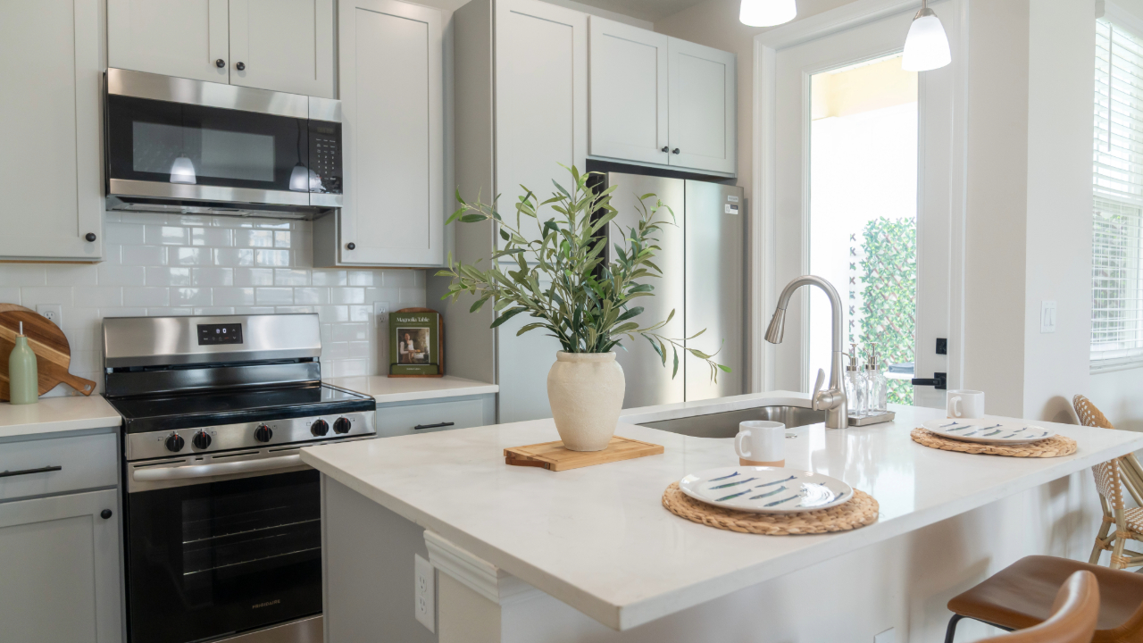 Home kitchen with a large white island with a sink and bar seating, looking into the living room, at The Eleanor Daytona Beach in Daytona Beach, Florida.