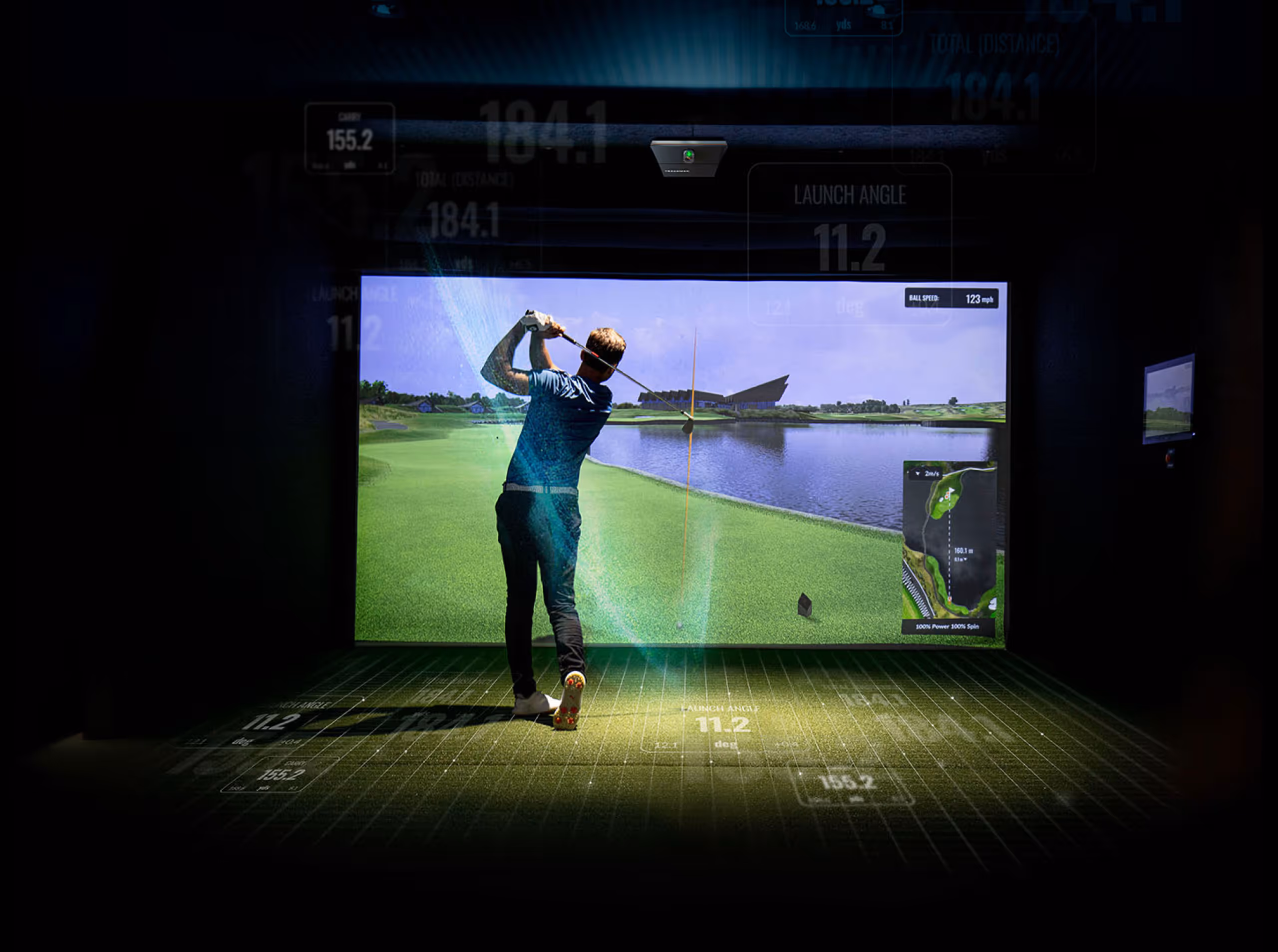 Person playing golf in an indoor golf simulator with a large screen showing a golf course.