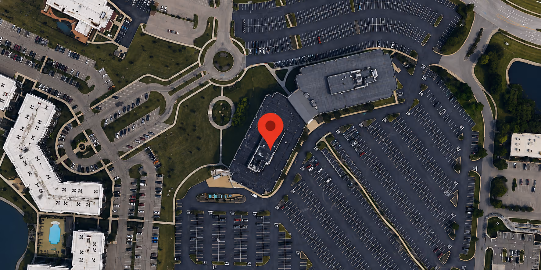 Aerial view of office buildings with a large parking lot and surrounding green spaces.