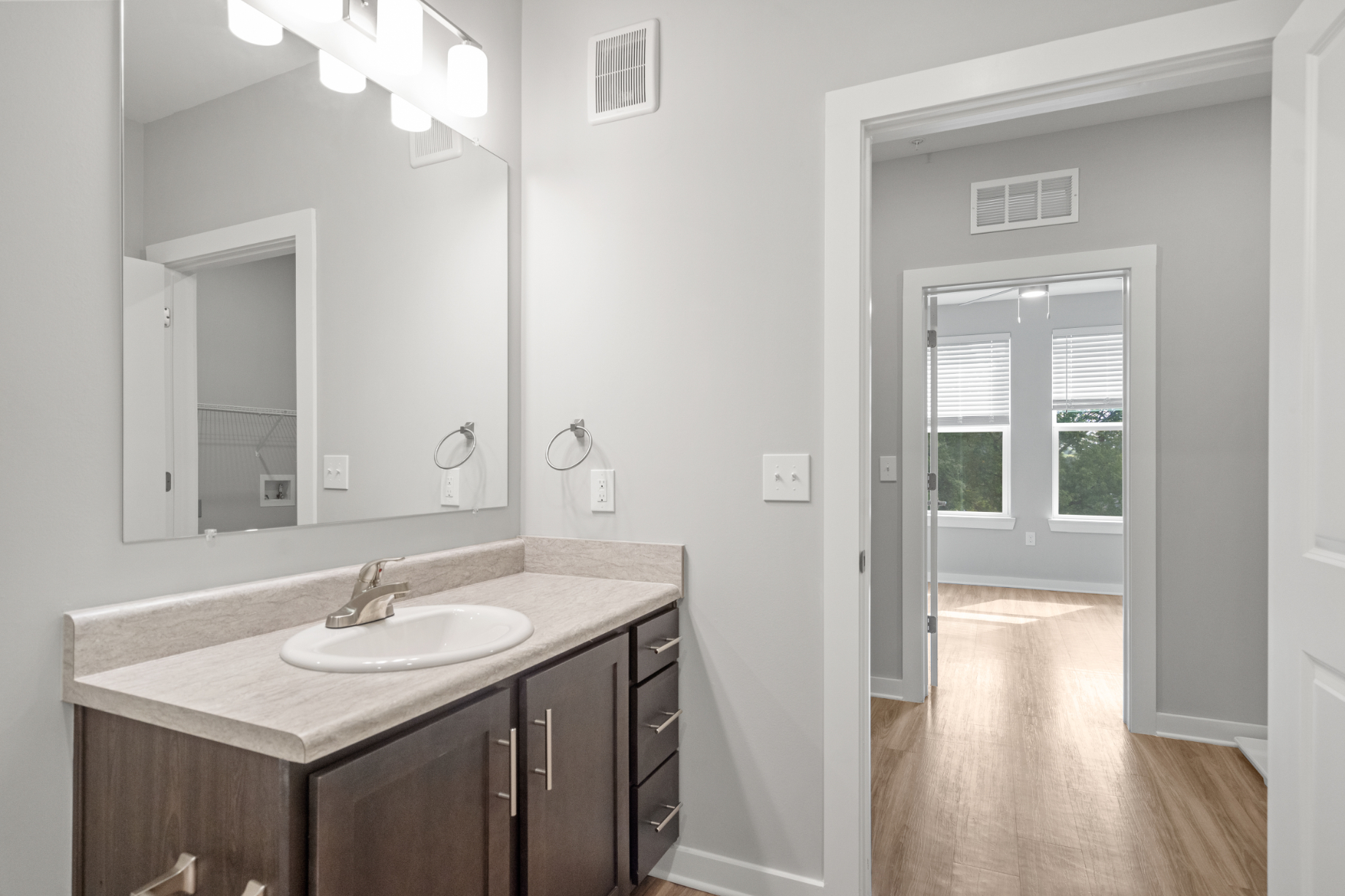Bathroom with brown cabinets, vanity, and view into unfurnished bedroom