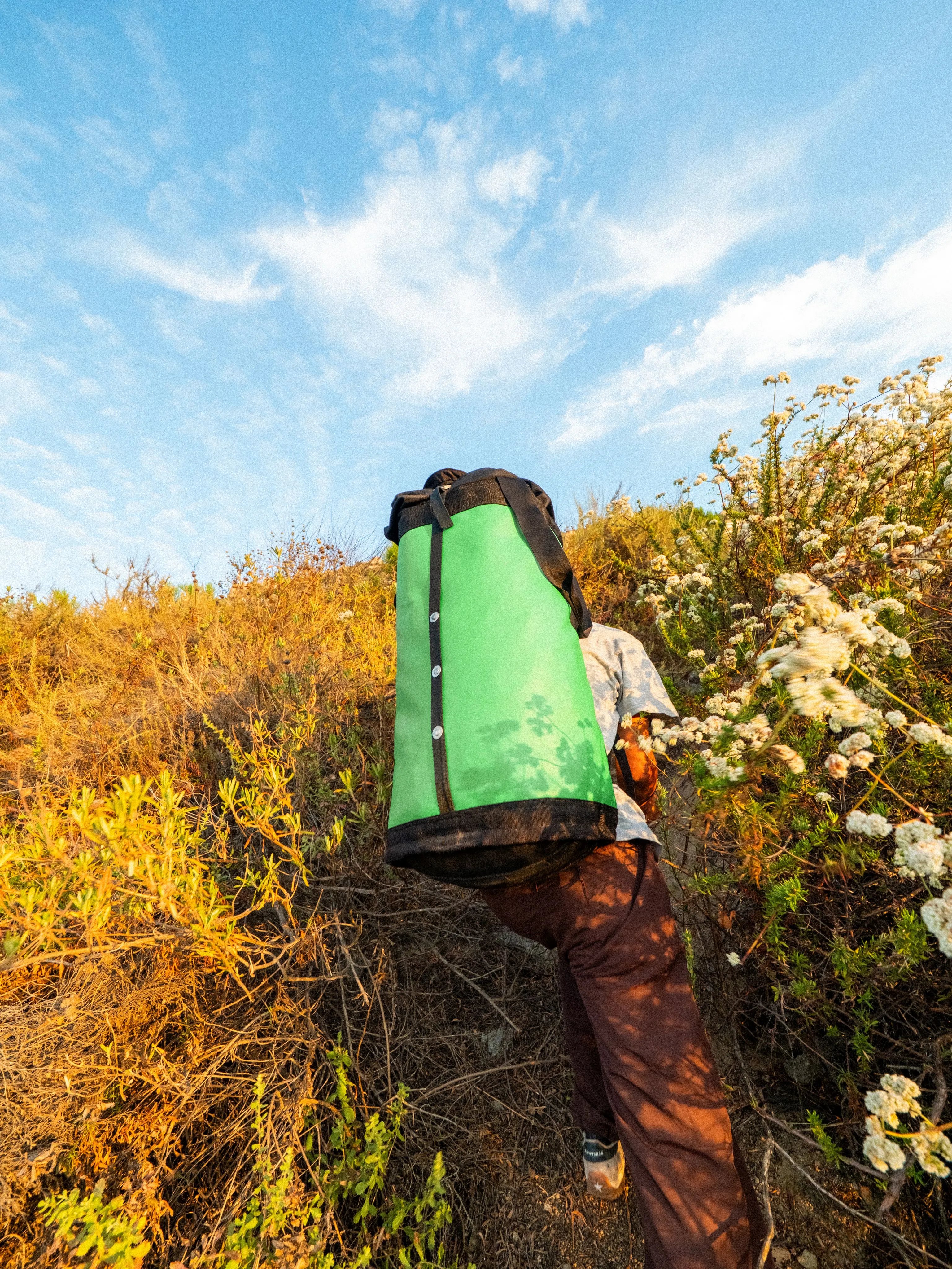 Green climbing bag carried through dry grass on a hillside, photographed by Kanyon Studio