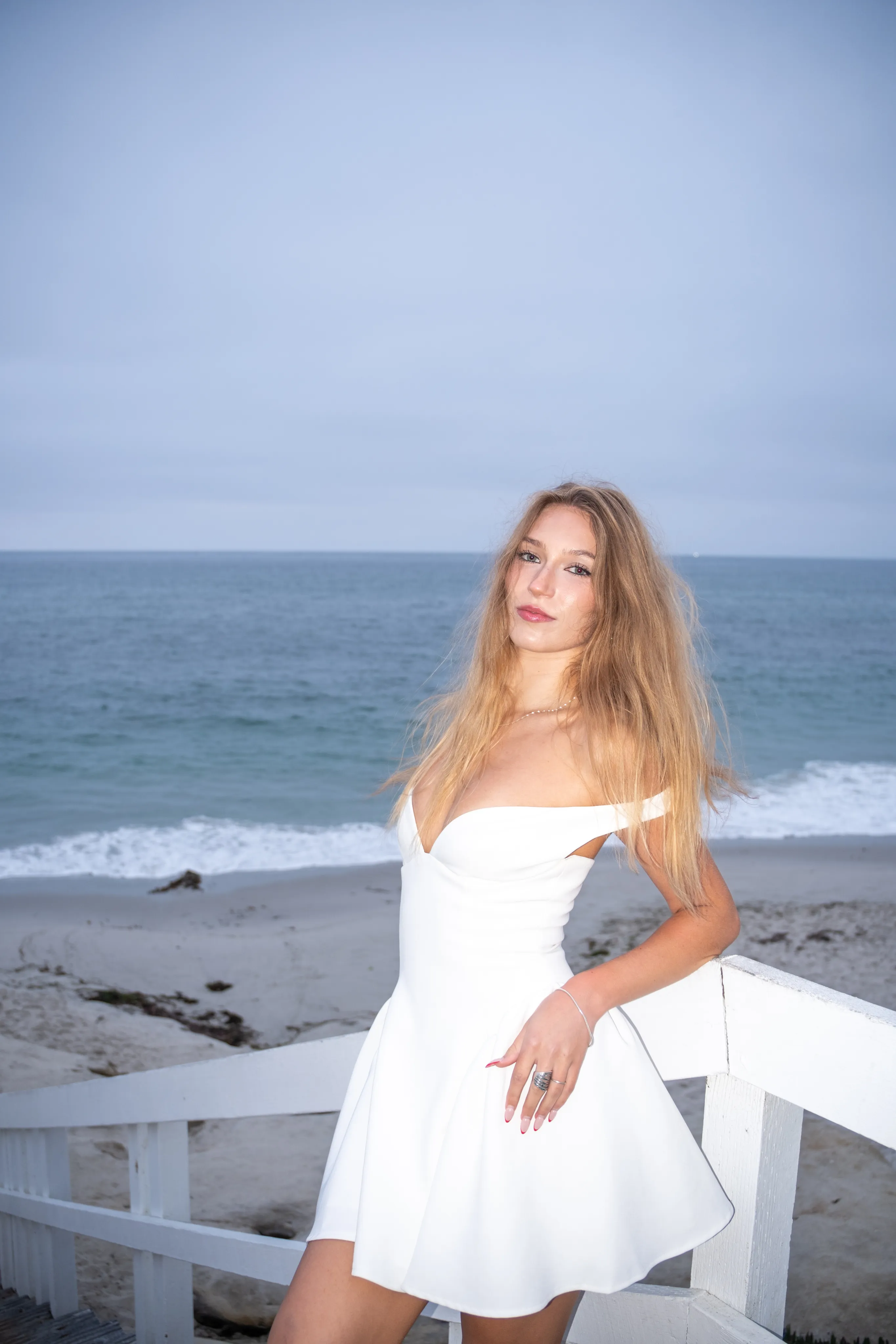 Portrait of a woman in a white dress beside a railing overlooking the ocean