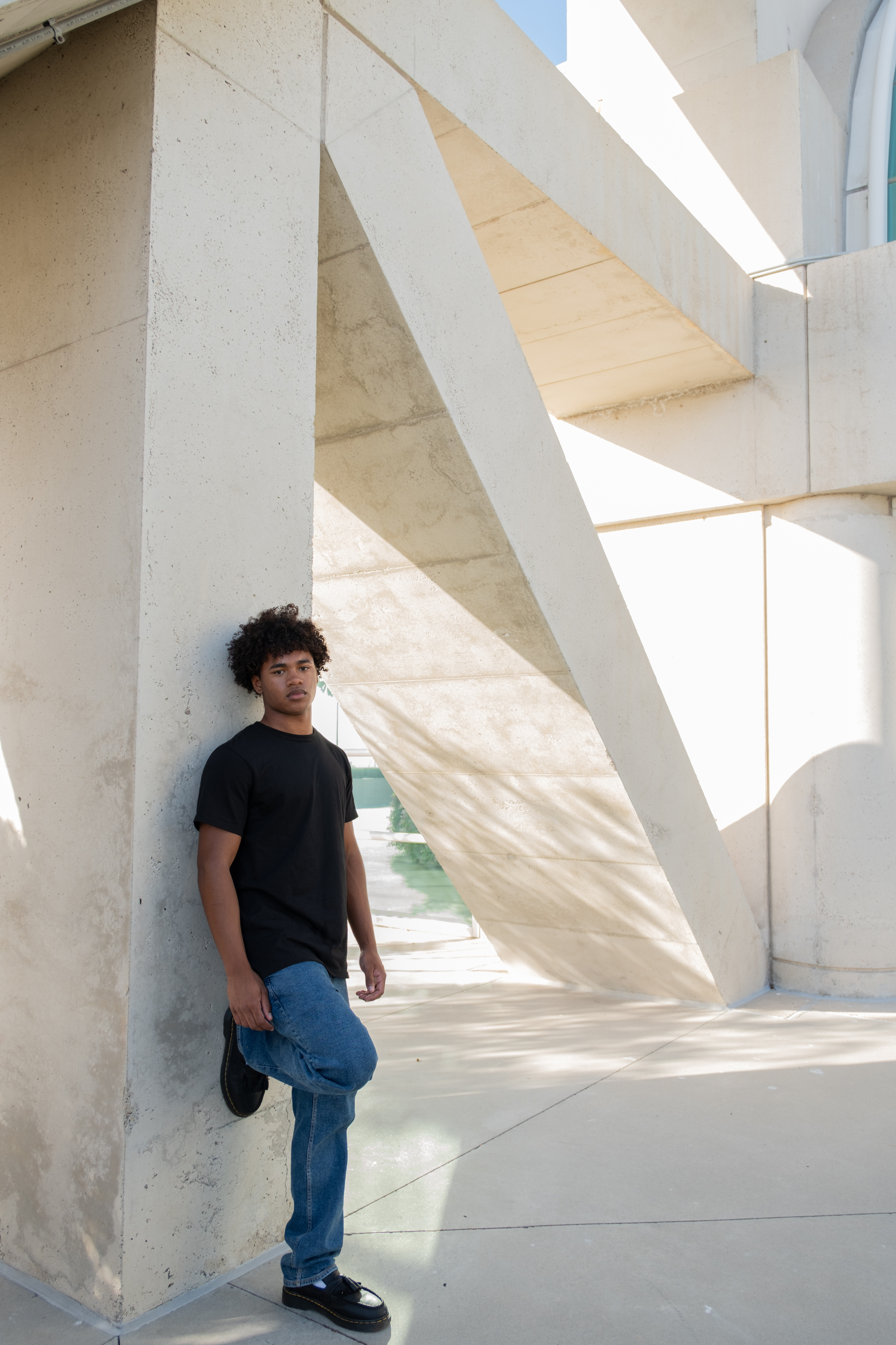Full-length portrait of a model in a black T-shirt and jeans leaning against a concrete wall