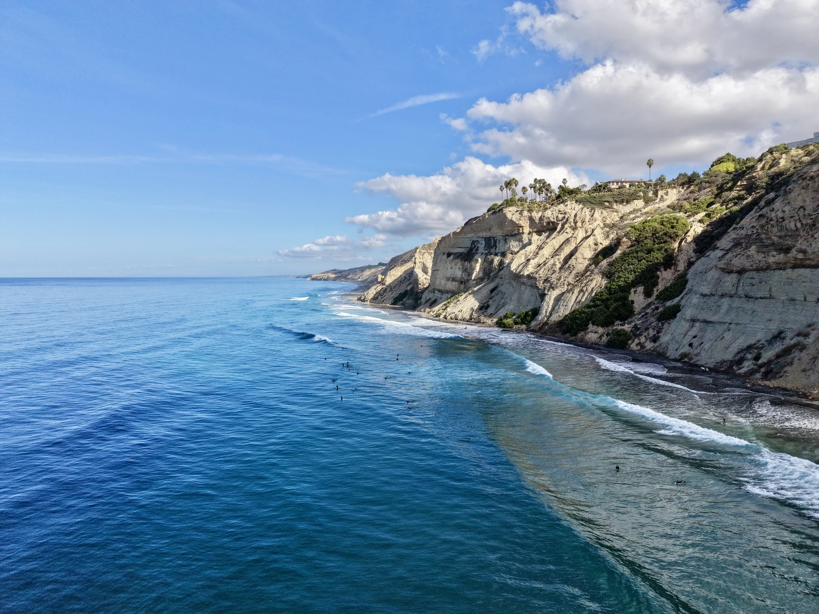 Coastal cliffs, breaking waves and surfers photographed from above the ocean