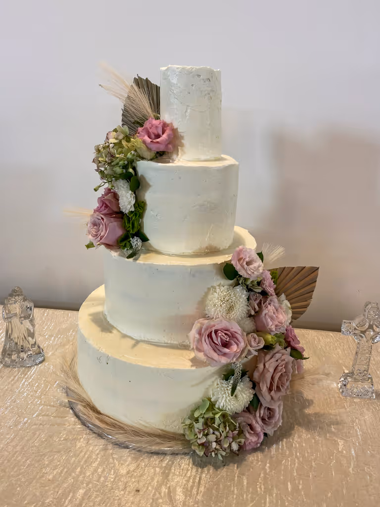 Four-tier white wedding cake with cascading dusty pink roses and wheat by Villani's Bakery
