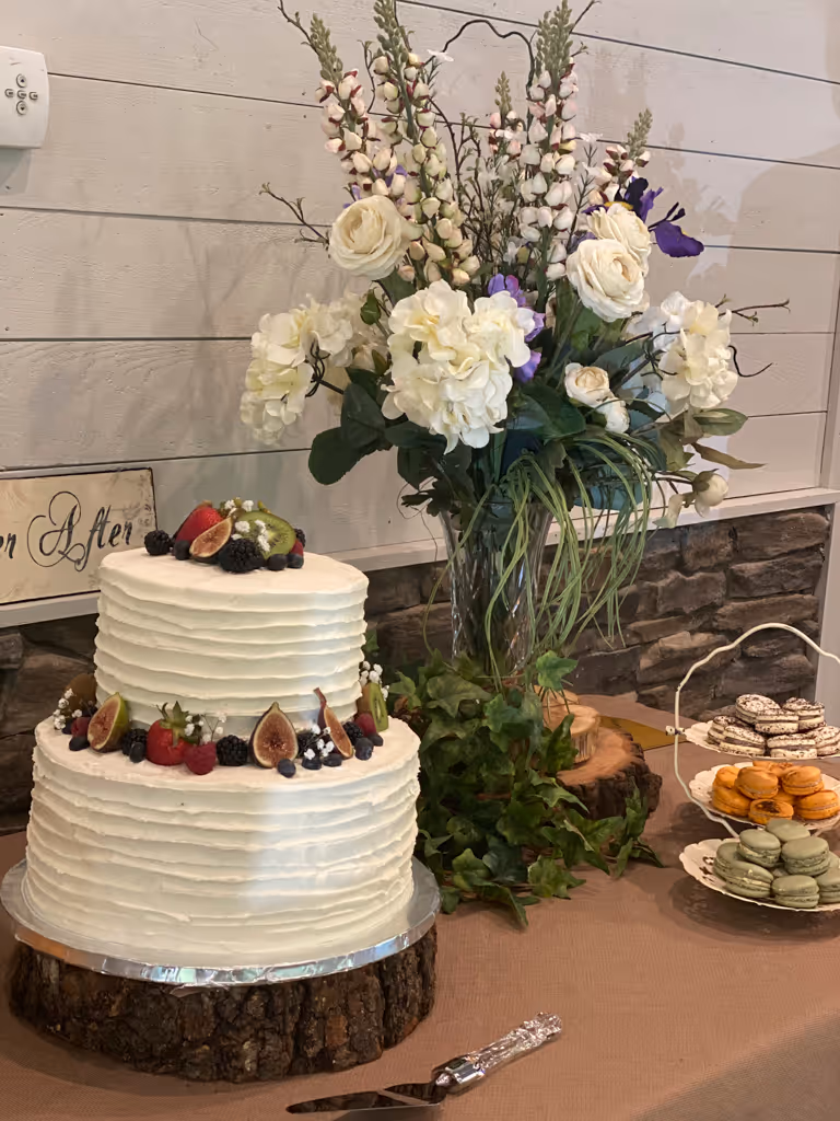 Two-tier white wedding cake with fresh berries on rustic wood stand by Villani's Bakery