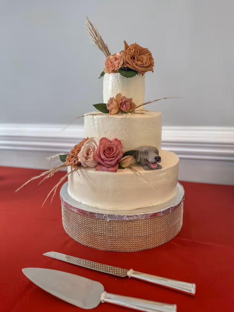 Three-tier white wedding cake with dusty rose flowers and wheat accents by Villani's Bakery