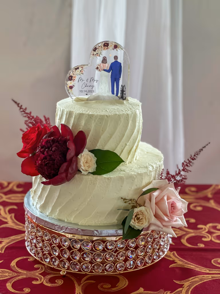 Two-tier white textured wedding cake with burgundy flowers and custom photo topper by Villani's Bakery