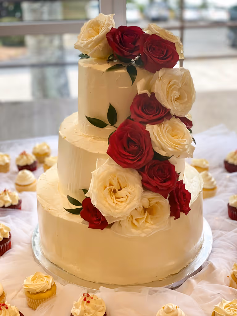 Three-tier white wedding cake with cascading red and cream roses by Villani's Bakery