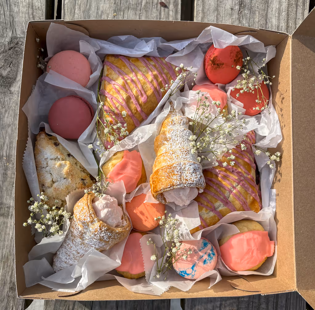 Assorted pastries and cookies in a bakery box, decorated with baby’s breath — by Villani’s Bakery.