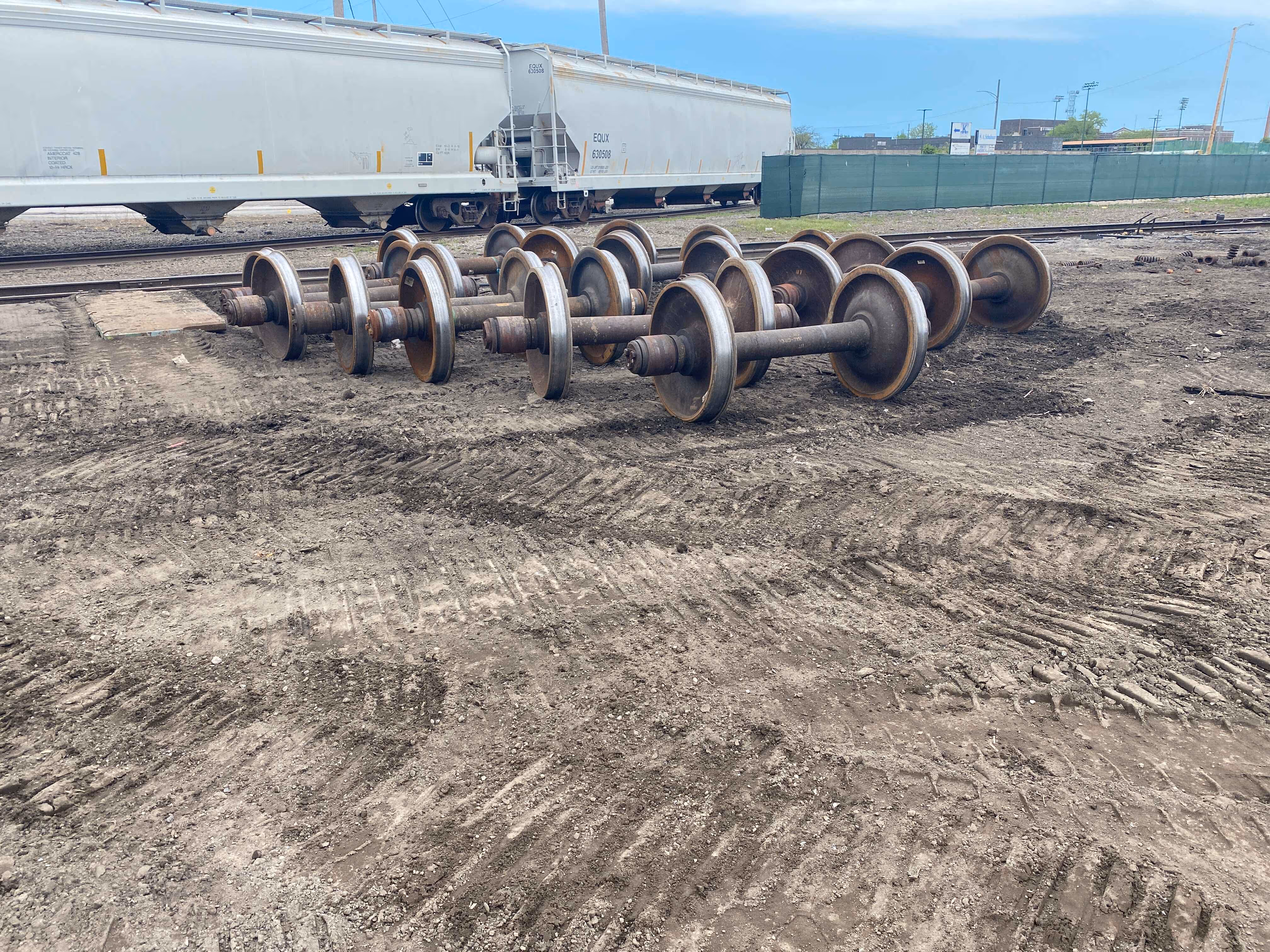  A pile of various wheels resting on a dirt field under clear skies.