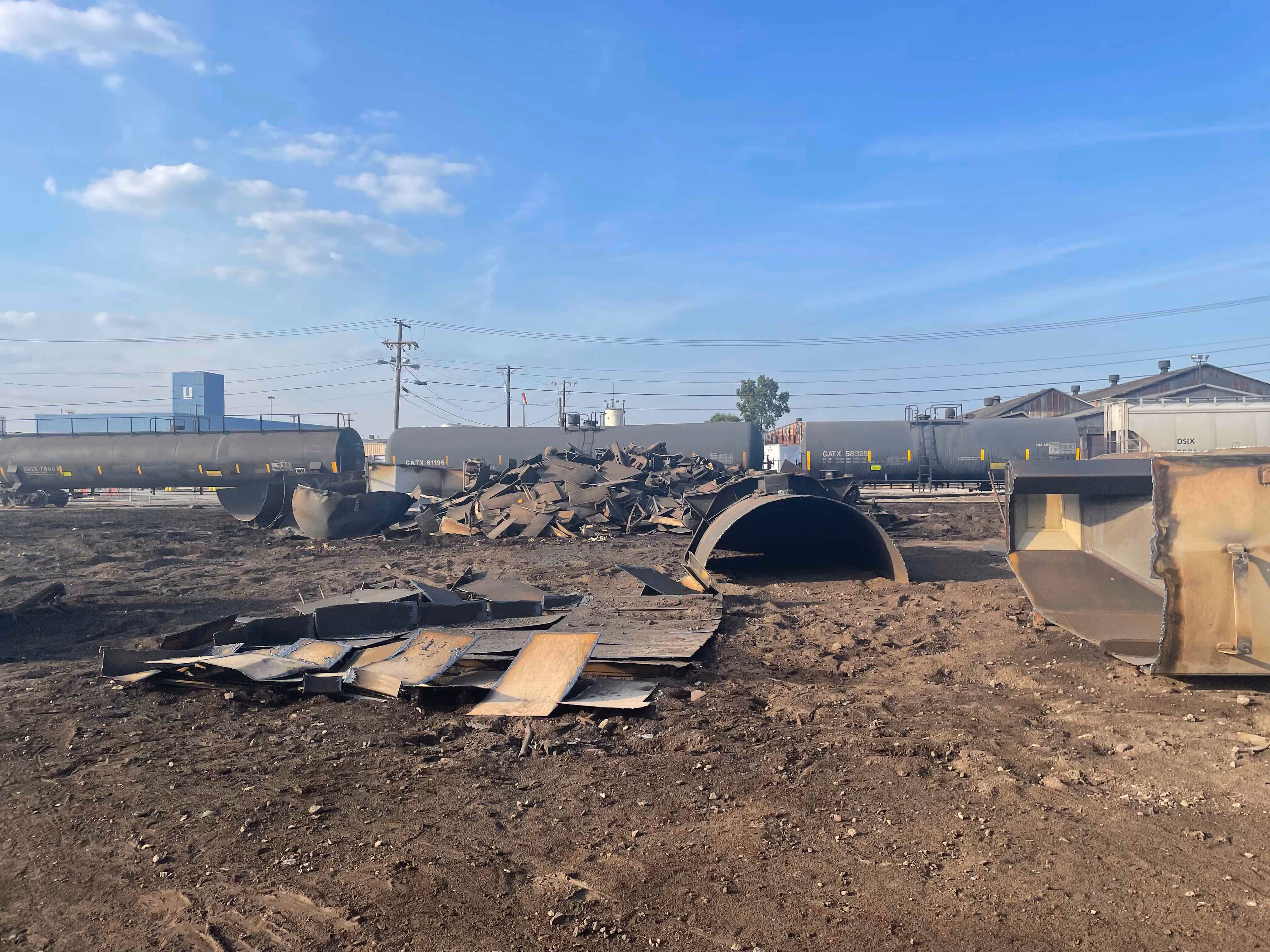 A tanker, a metal tank and some metal scraps lying around in a dirt field.