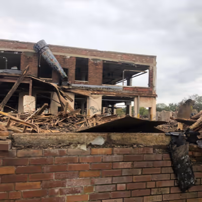 A broken brick wall in front of a house  being taken down.
