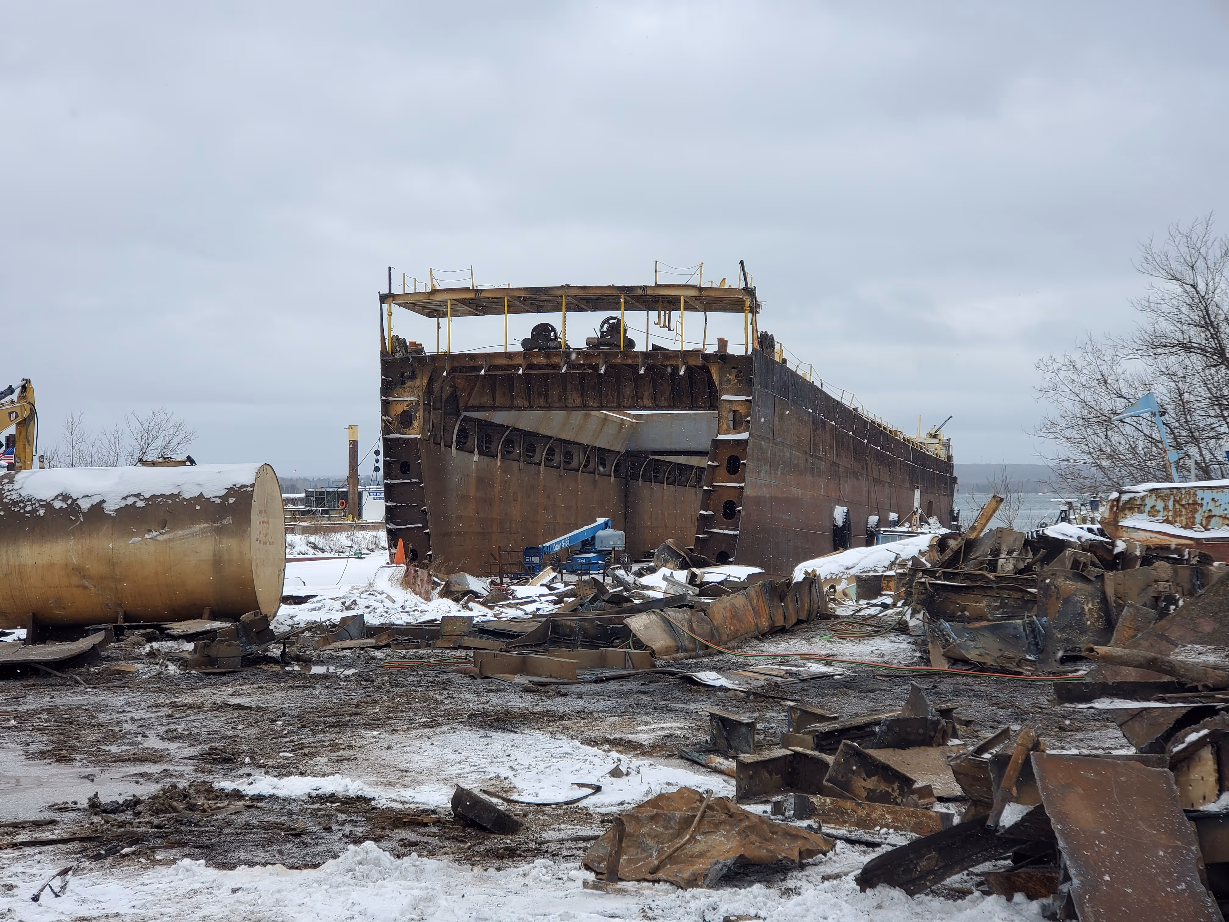 Half of a very large rusted ship sitting on land.