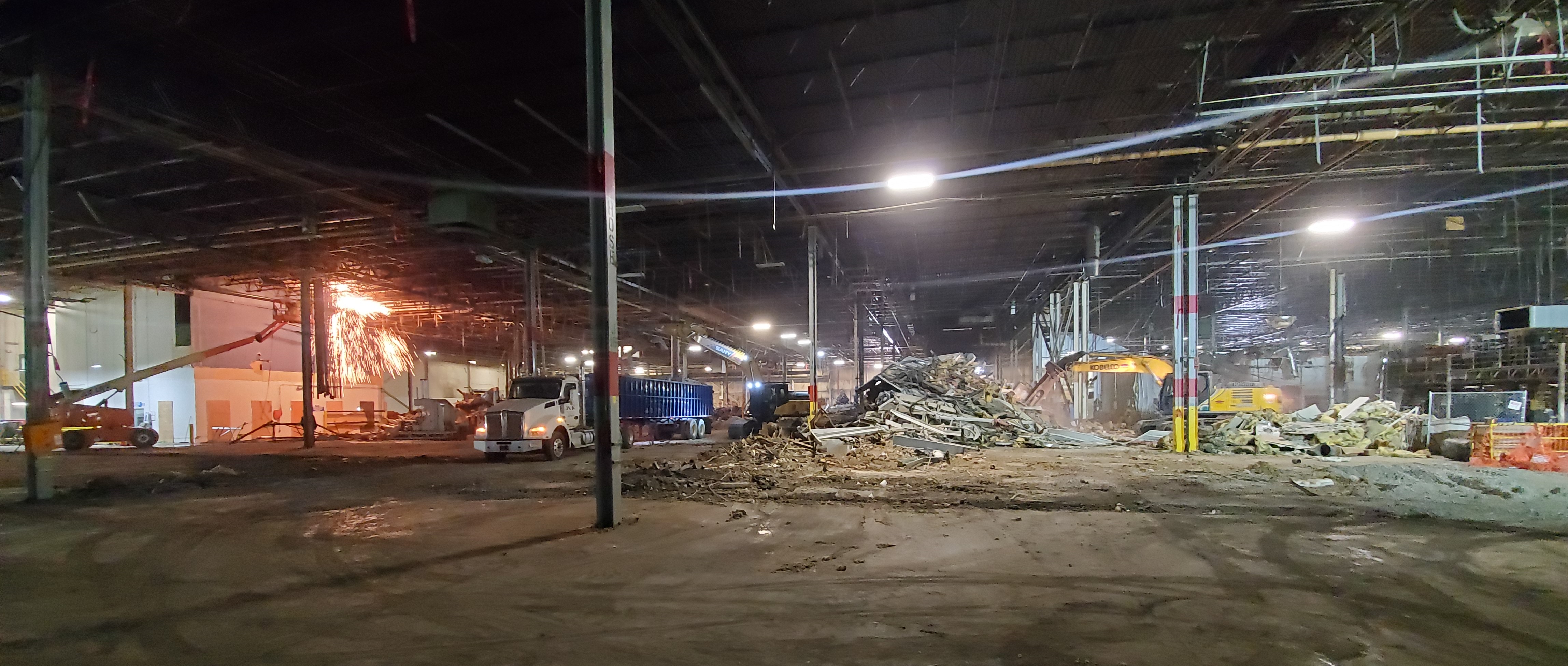 Nighttime demolition work at an industrial facility with floodlights illuminating the site