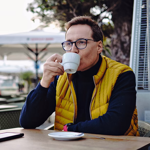 A man sitting at a table drinking a cup of coffee.