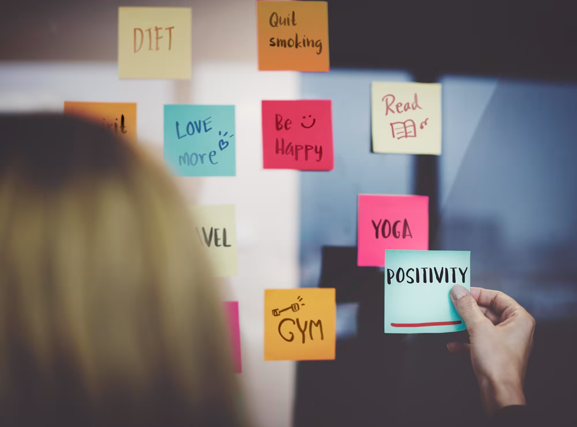 A woman holding a coffee mug in front of a wall with sticky notes on it.