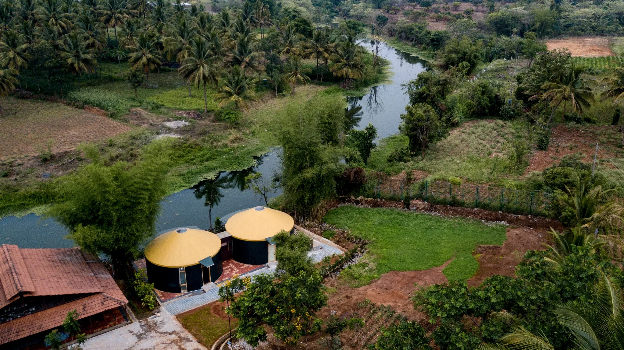Aerial view of eco-resort with yellow-roof yurts surrounded by lush greenery and a winding river.