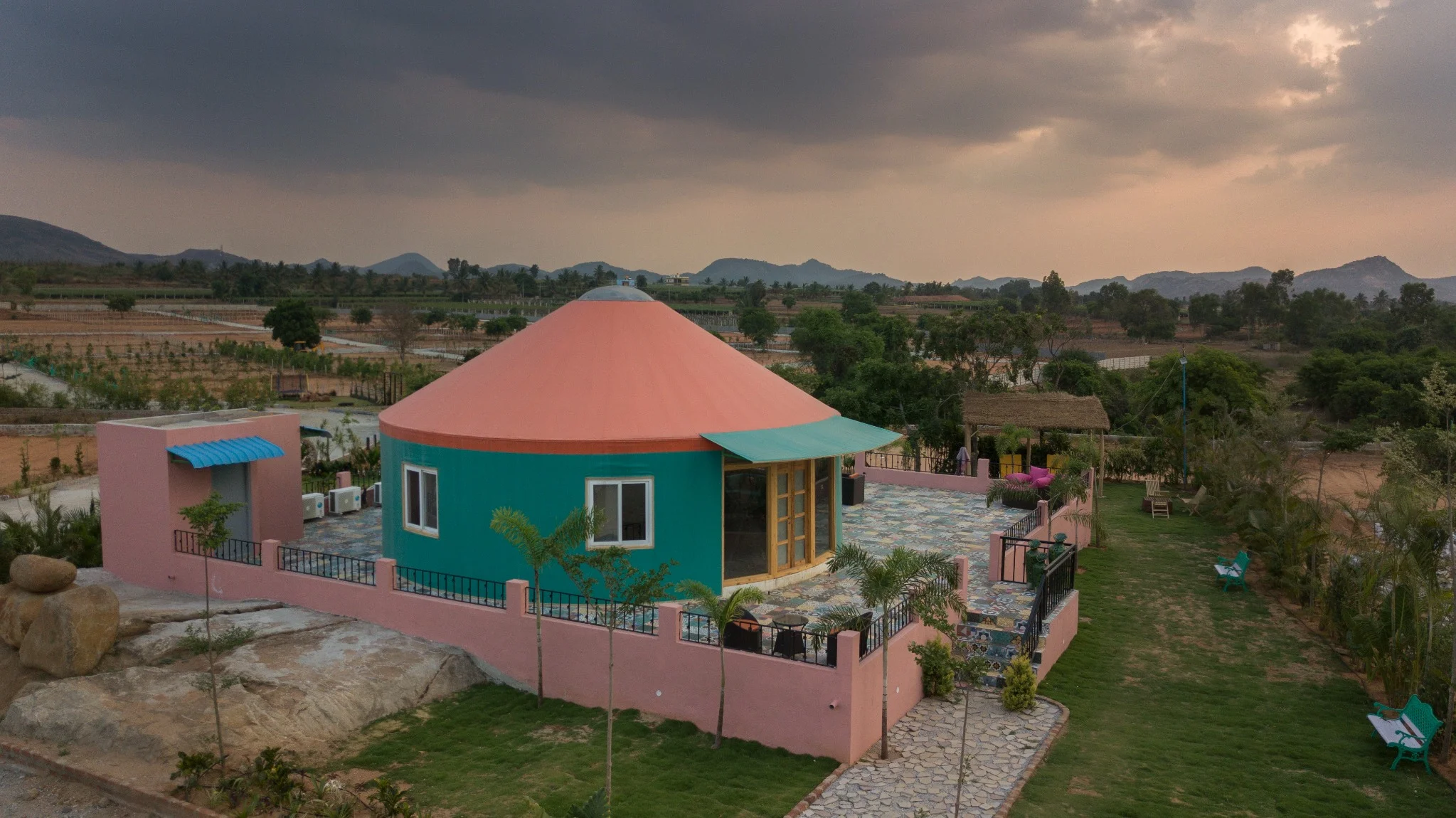Scenic exterior view of a colorful eco-resort yurt surrounded by greenery and mountain ranges.