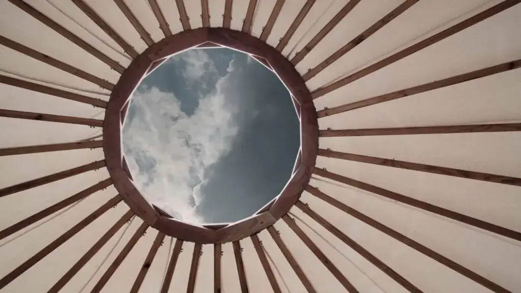 View from inside a yurt showing wooden beams and a circular opening to the sky