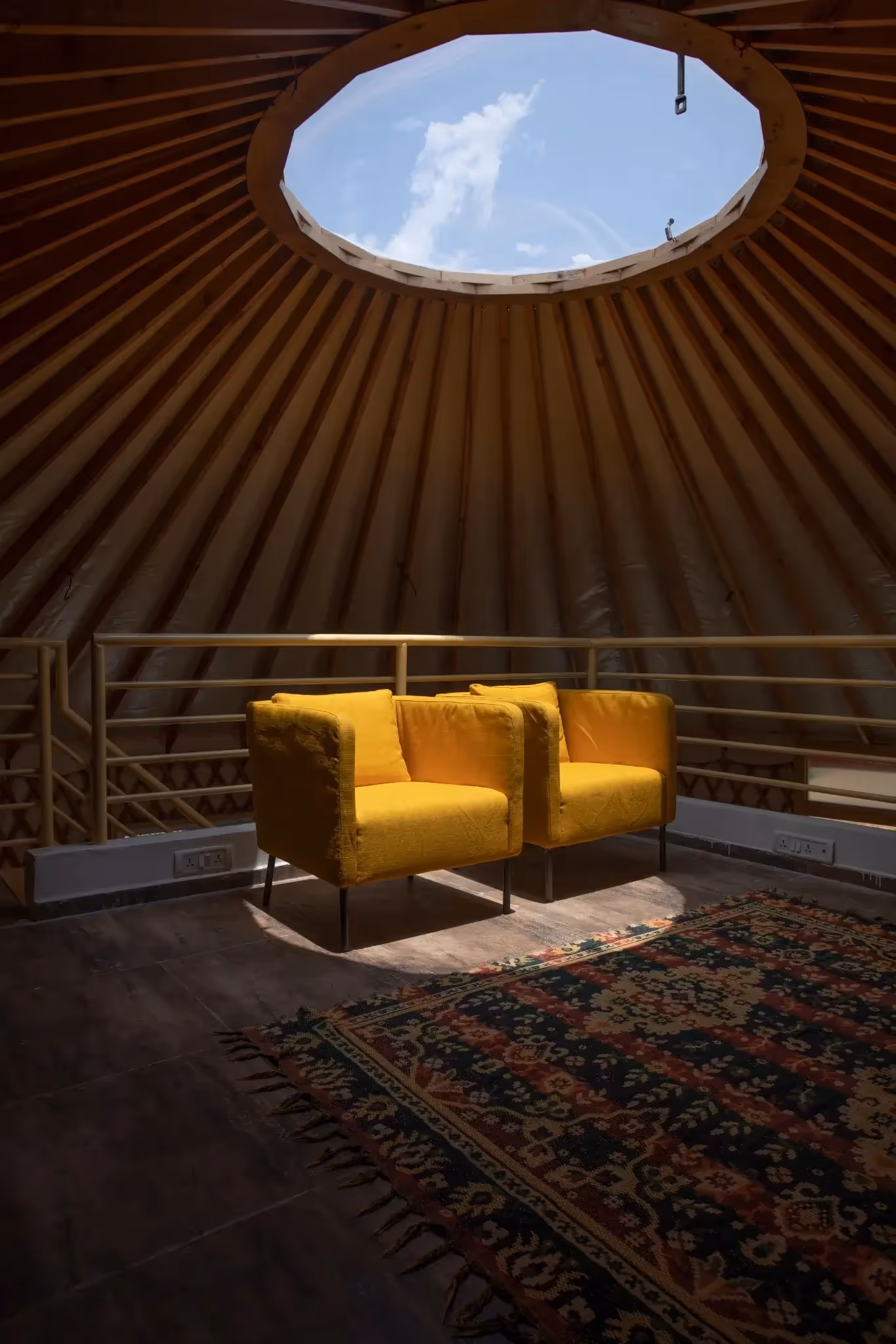 Cozy mezzanine seating area inside a yurt with skylight and warm sunlight.