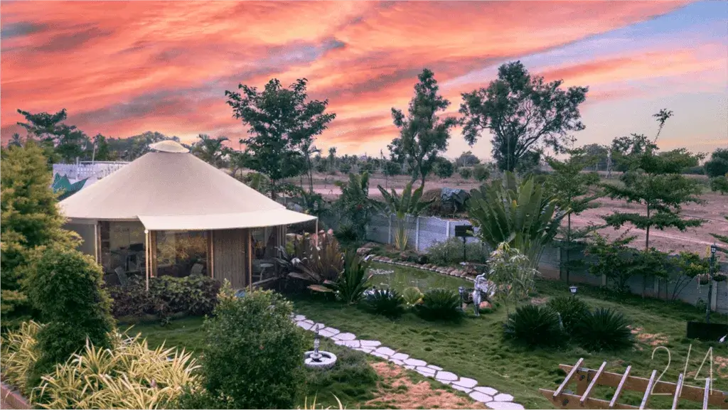 A cozy yurt surrounded by lush greenery and a colorful sunset sky