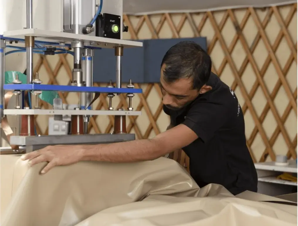 Worker operating a machine, preparing materials inside a yurt workshop environment
