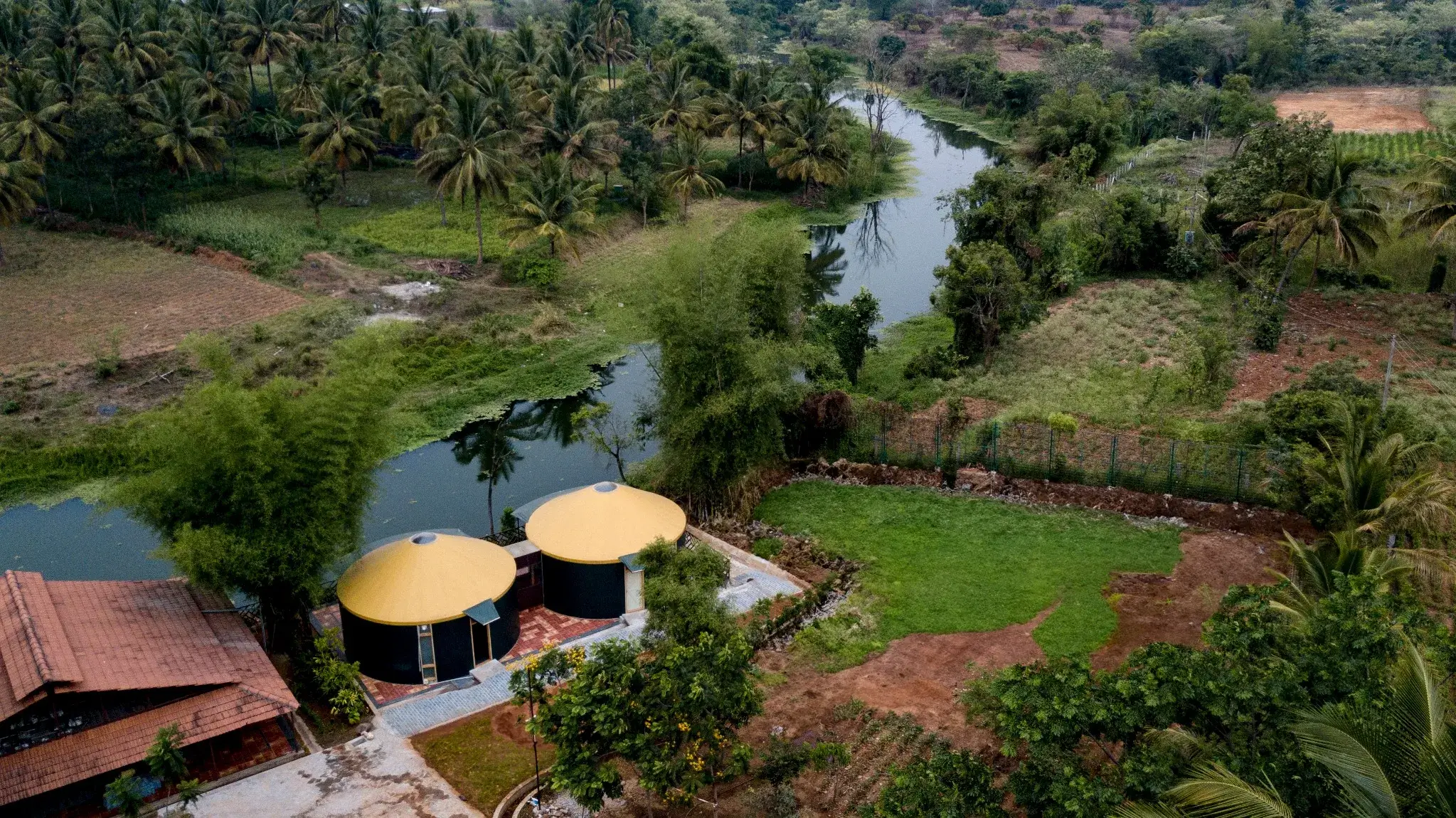Aerial view of eco-resort with yellow-roof yurts surrounded by lush greenery and a winding river.