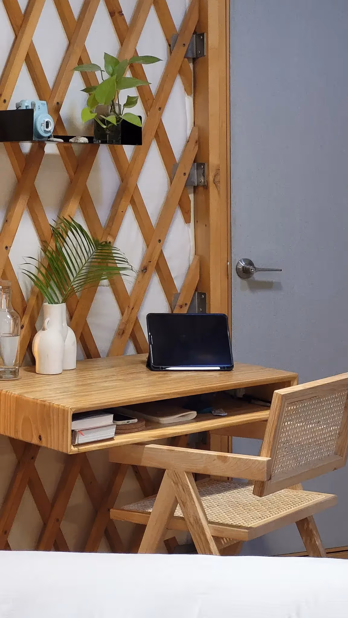 Minimalist yurt workspace with a wooden desk, woven chair, indoor plants, and a cozy, sustainable design.